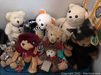 Photo showing a tub containing 10 different collectible plush bears. Various colors and styles visible including white, tan, brown, and black plush bears with some wearing clothing and accessories. Several bears have collector tags attached.
