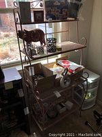 Full view of the metal bakers rack in a room, showing three shelves with various small items and visible scratches on the metal frame.