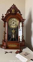 Front view of mahogany arched cabinet clock with carved crest, brass figurines and keys on table