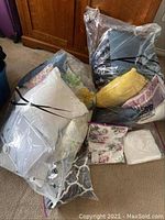 Two transparent vacuum-sealed bags containing queen-sized bedding sets, one with floral and white fabrics, and the other with darker tones including gray.