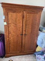 Front view of large wooden armoire cabinet with double paneled doors and round metal knobs.