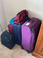 Side view of six pieces of luggage including rolling suitcases in purple, blue, red, and two duffel bags on top