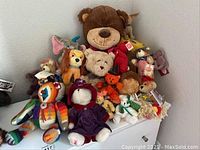 Overall view of 13 different teddy bears and plush animals on a white base, showcasing various designs, sizes, and outfits.