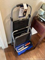 Two step stools stacked including one folding one with tag and one smaller metal stool. Blue toolbox with hand tools below them.