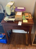 Singer sewing machine on top of wooden cabinet with accessories nearby