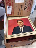 Framed photo of John F. Kennedy in red background labeled 'John F. Kennedy 35th Memorial Issue'.