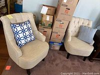 Photo showing both beige tufted armchairs with two decorative pillows and surrounding packing boxes