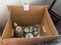 A box containing the coffee pot, matching cups, and tiles covered in cushioning materials for protection during transport.