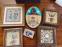 Six framed Navajo sand paintings displayed on wooden surface, showing variety of traditional motifs and colors