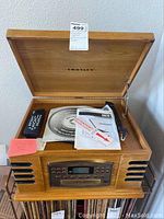 Open wooden Crosley CR79 entertainment center showing record player, remote control, and manuals inside.