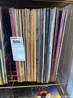 Photo showing a vertical row of 40 vinyl LP albums in a metal rack, spines showing various artists and titles.