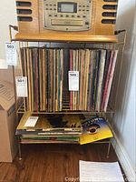 Brass record player stand holding multiple vinyl records, revealing gold-colored metal with scratches and wear.