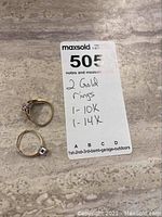 Overhead shot of two gold rings next to note stating 1-10K and 1-14K