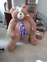 Full body image of large 51 inch Vermont Teddy Bear sitting on floor with patriotic scarf, showing size and general condition.