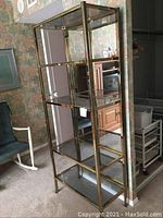 Glass shelving unit angled view showing bronze metal frame and multiple glass shelves with a mirror back reflecting surrounding room.