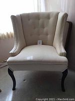 Front view of the cream oversized wingback chair showing tufted backrest and winged sides.