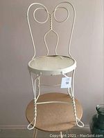 Full view of antique cream-colored metal vanity chair showing ornate metal backrest and twisted leg design.
