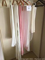 Photo of several hanging linens in white, cream, and pink fabric, likely runners or tablecloths.