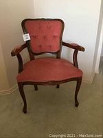 Front full view of antique armchair showing carved wooden frame and pink tufted upholstery