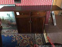 Wide photo showing the Stanley cabinet with both side extension wings fully opened, wood finish visible along with rug and wall decor behind it.