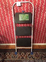 Front view of step stool showing three black textured steps, white frame, blue foot caps and Safety 1st branding on top step.