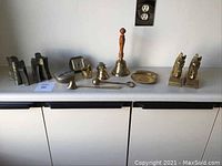 Wide shot showing all brass items aligned on a cabinet surface including bookends, bells, dishes, and other small brassware