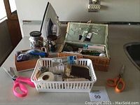 Photo showing the sewing accessories including scissors, jars of thread, sewing basket and white plastic basket