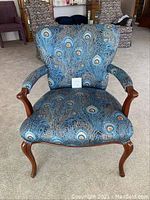 Front view showing blue peacock feather patterned upholstery and carved wooden arms and cabriole legs