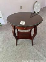 Oval side table with a dark wood finish, glossy glass top, and curved legs shown from the front.