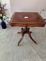Full view of antique wooden end table showing embossed leather top with intricate gold detailing and scalloped wooden edge.