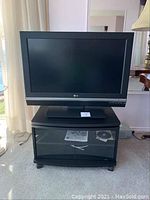 Front view of the LG TV on top of the black glass-door TV stand showing the overall setup and condition.