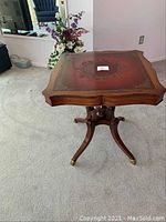 Full view of antique end table on carpet with background furniture and flowers.