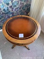 Top view of the round end table showing leather inset with gold detailing and wood grain outer ring.