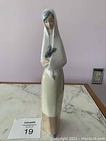 Front view of the tall slender porcelain figurine showing the woman holding the gray rabbit
