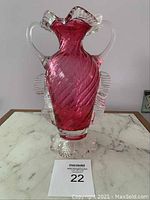 Front side of rose pink glass vase with clear handles and decorative clear ruffled borders on sides and base.