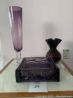Top-down and angled shots of the three mauve glass items displayed on a marble-topped table: tall vase, ruffled smaller vase, and ornate square dish.