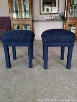 Front view showing two blue square vanity stools with cushioned seats and four legs, covered in dark blue fabric with zigzag pattern, standing on carpeted floor.