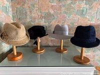 Four hats displayed on seven wooden stands against a decorative background.