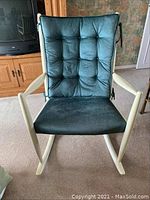 Front view of oversized rocking chair showing tufted green cushion and cream wooden frame.