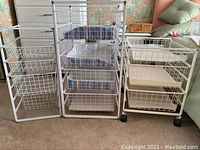 Front view showing three white metal closet organizing racks with multiple wire baskets positioned side by side on carpeted floor.