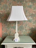 Single lamp photo showing full lamp with rectangular white fabric shade and decorative cream-colored base on glass table.
