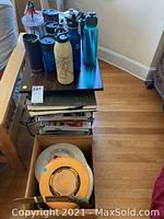 Photo showing assortment of water bottles in different colors and materials placed on small table near crate containing Frisbees.