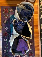 Photo showing three paper bags filled with women's clothing in blue, black, and purple colors on a floral rug.