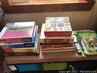 Stack of assorted jigsaw puzzles including Pomegranate brand and Doctor Zhivago puzzle, Momo the Dog puzzle, various boxed puzzles, and two Crazy Cat Lady action figures still in their packages beside two model train pieces on a table.