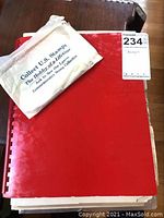 Red comb-bound album closed with an envelope on top stating 'Collect U.S. Stamps The Hobby of a Lifetime'