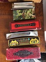 Top view of six vintage harmonicas including Echo Harp, Chromonika, Opera in original cases showing wear and rust