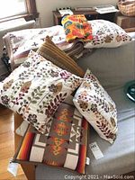 Wide view of Pendleton blanket with Southwestern pattern and several throw pillows on a couch and chair, showing patterns and condition including hole in blanket.