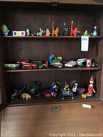 Full view of three shelves with assorted figurines, die cast cars, wind-up toys, and buses.