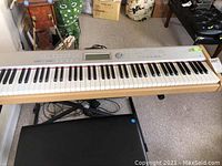 Full view of keyboard on X-stand with bench beneath and cables visible