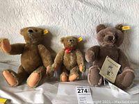Three Steiff teddy bears of varying sizes with yellow ear tags, posed sitting on a surface with a MaxSold tag visible.